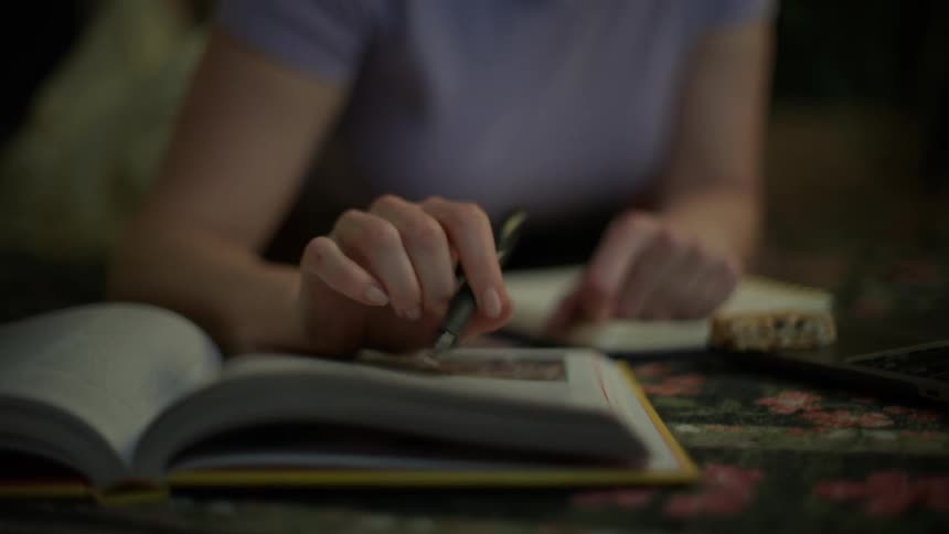 A focused young woman in glasses studies on the floor at night, using her laptop and books in a cozy, dimly lit room
