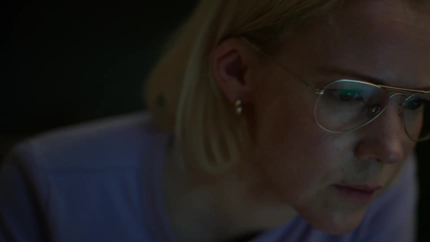 A focused young woman in glasses transitions from flipping through a textbook to working on her laptop late at night