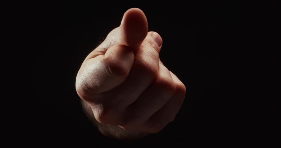 A dramatically lit hand slowly forms the rude 'fig sign' gesture against a black background