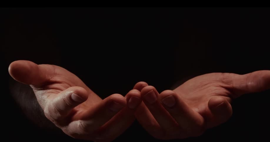 Cupped hands open and close in a dramatic beam of light against a dark background