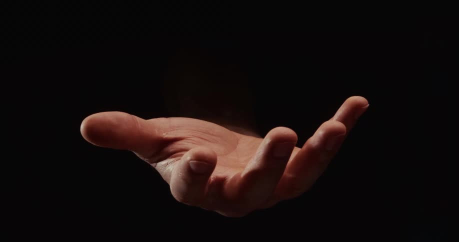 A single hand slowly emerges from the darkness, opens its palm up to the light, and then closes before disappearing