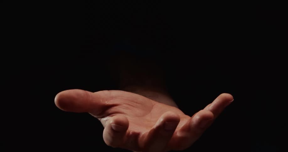 A hand emerges from the darkness, slowly opening its palm in a gesture before clenching into a fist