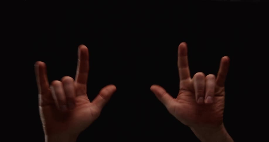Close-up of two hands making the rock and roll gesture against a dark background