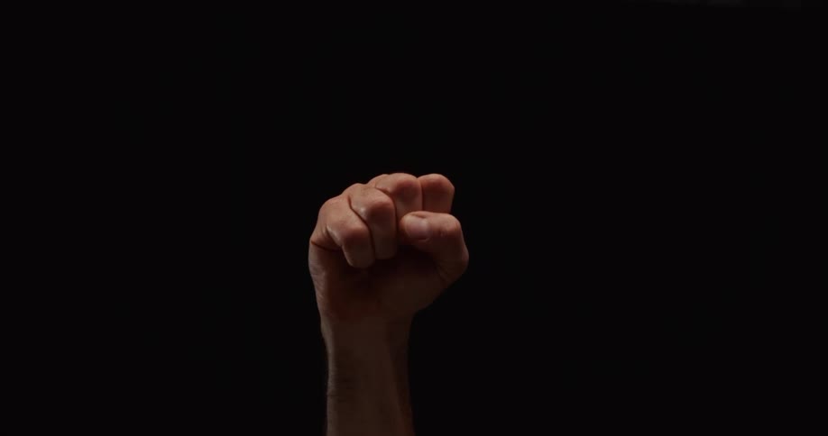 A man raises his clenched fist high in a symbol of protest and solidarity against a solid black background