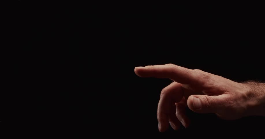 A dramatically lit male hand with a pointing index finger is isolated against a solid black background