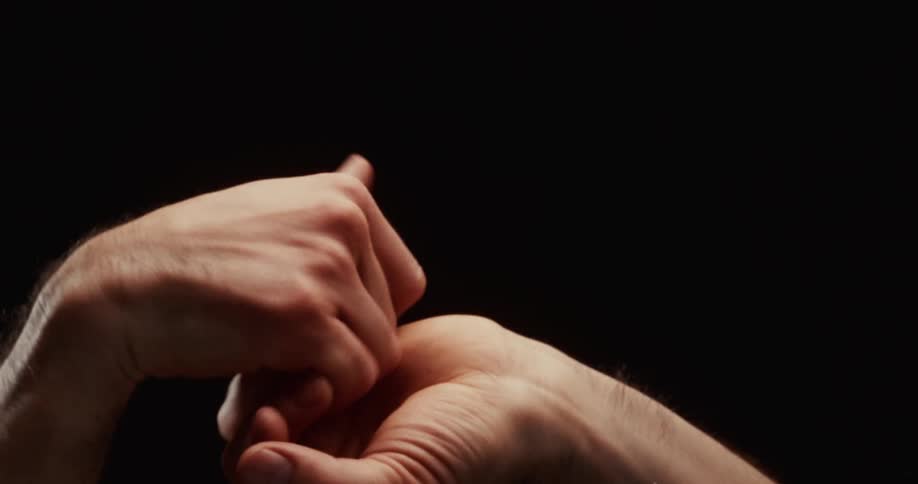 Dramatic closeup of two male hands slowly and gracefully intertwining their fingers against a black background
