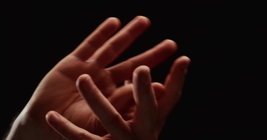 Expressive male hands intertwine and dance gracefully in slow motion against a solid black background