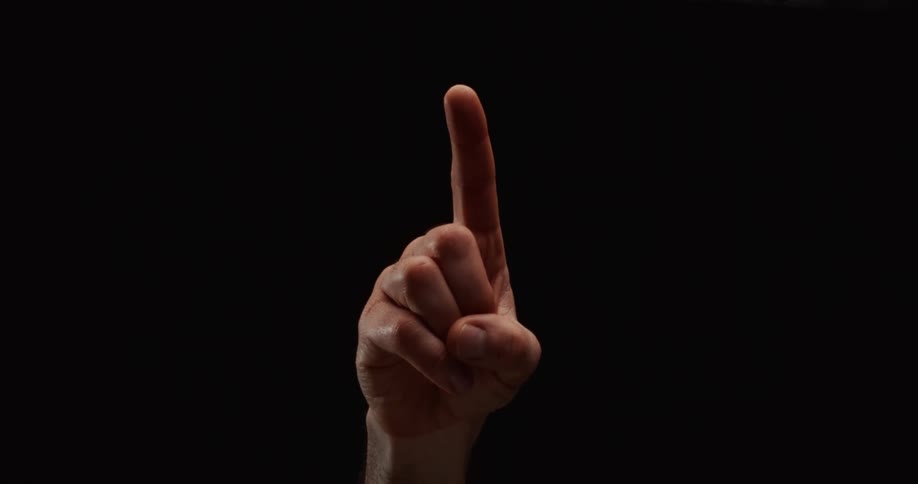 A male hand emerges from the darkness to raise one finger, counting or making a point against a solid black background