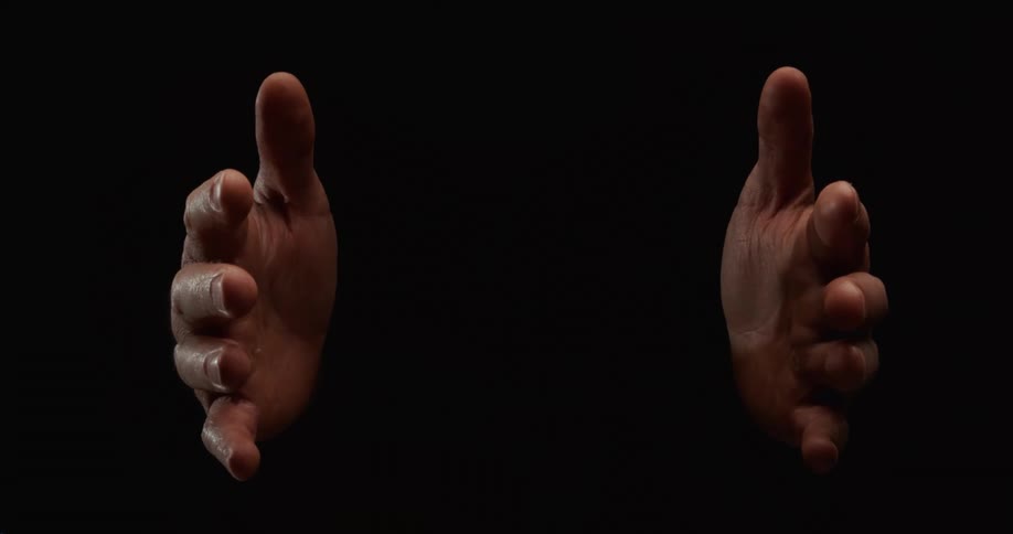 A pair of hands mysteriously emerges from the darkness, slowly opening to present an invisible object before closing and disappearing again