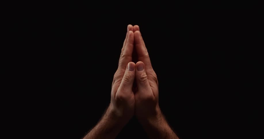 A closeup of a man's hands rising and coming together in a prayer position against a black background