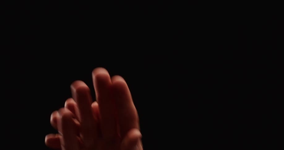 A close-up of a pair of hands moving gracefully in slow motion, intertwining their fingers in an expressive dance against a black background