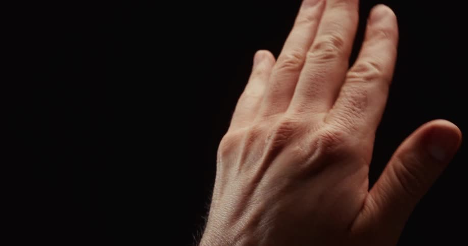 A dramatic closeup of a hand slowly and expressively closing into a fist and then opening against a black background