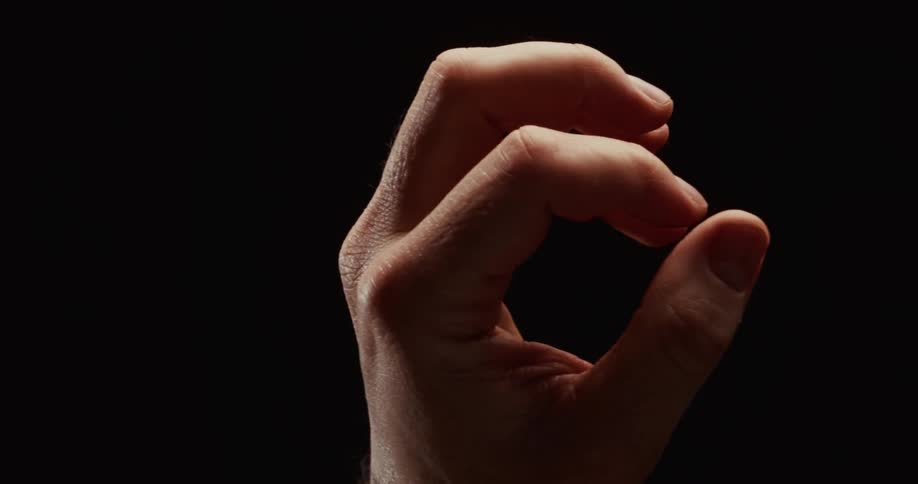 A man's hand slowly clenches into a tight fist in dramatic lighting against a black background