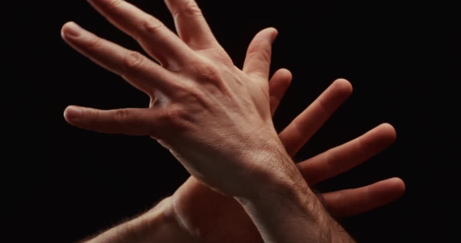 An artistic and dramatic close-up of two hands slowly unfolding and separating against a black background