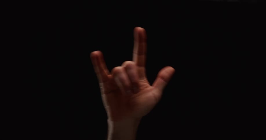 A hand makes the heavy metal rock and roll horns gesture against a stark black background