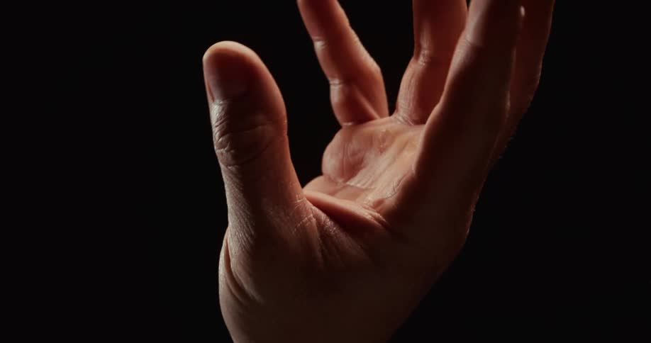 A tightly clenched fist slowly and dramatically unfurls into an open palm against a dark background