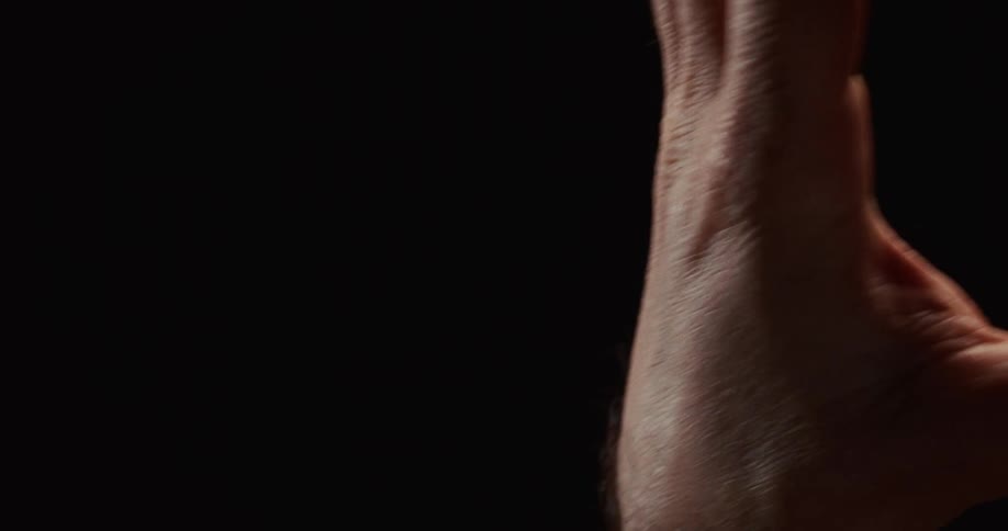 A dramatic close-up of a human hand slowly opening and closing into a fist against a black background