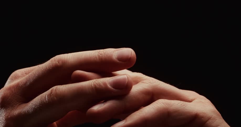A dramatic close-up of a person's hands with fingers intertwined, slowly shifting against a dark background