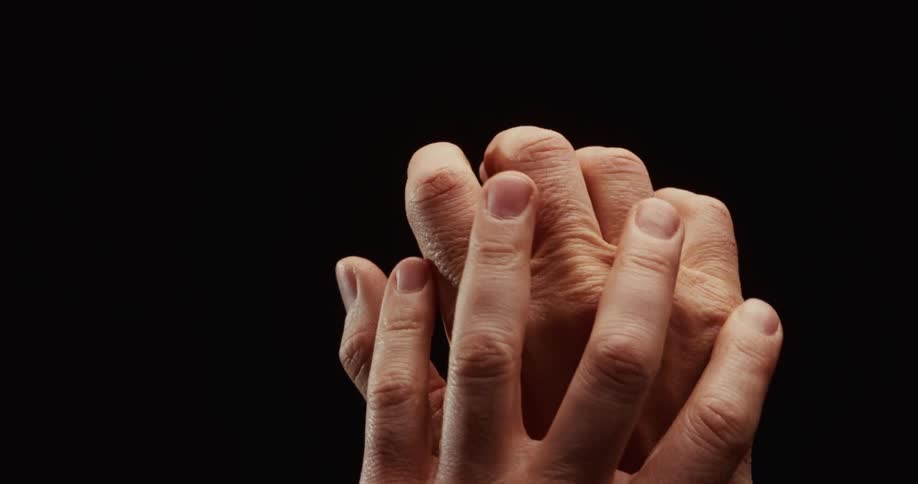 A young hand slowly and gently holds and caresses an older hand, symbolizing love, support, and compassion across generations
