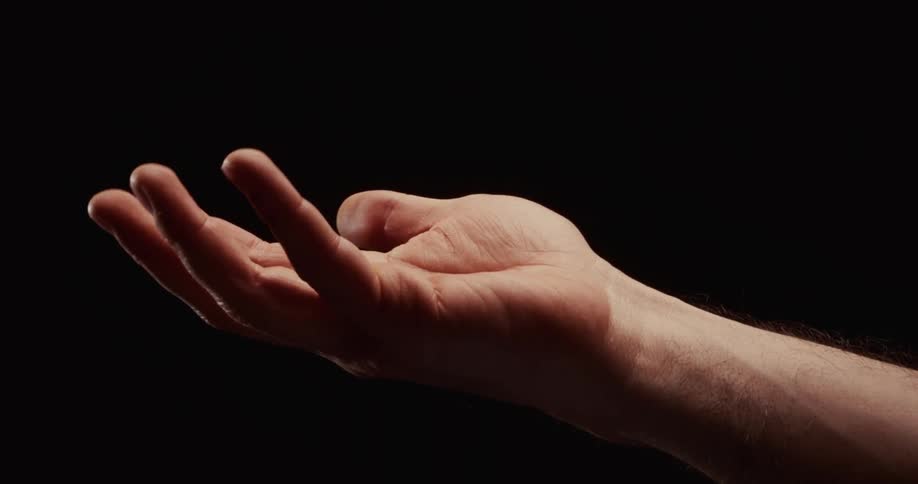 A man's hand slowly unfurls from a fist, opening up against a dramatic black background