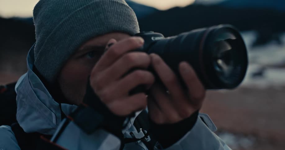Close-up of a determined male photographer in a beanie raising his camera to capture a shot in a cold outdoor environment