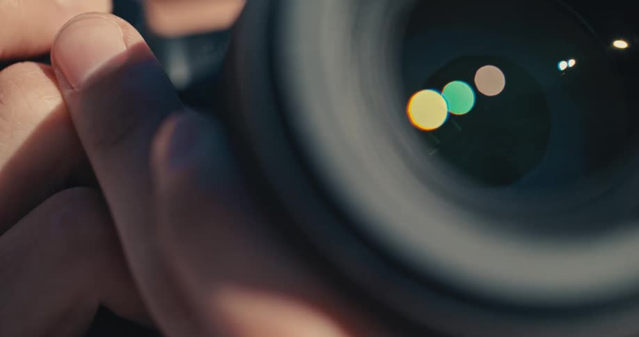An extreme close-up of a camera lens shows the aperture opening and closing, with colorful light reflecting on the glass