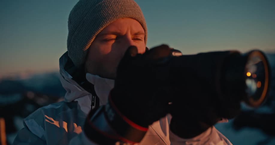 A professional photographer in winter gear captures the stunning golden hour light over a beautiful snowy mountain landscape