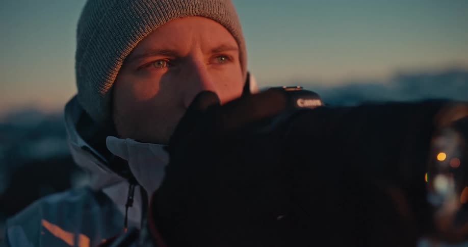 Slow motion close-up of a young male photographer taking pictures of the sunset with his professional camera in the snowy mountains