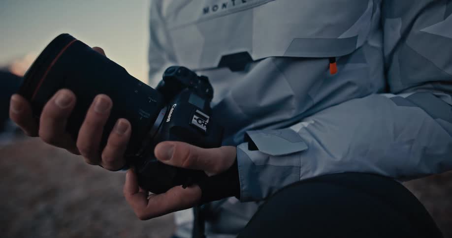 A photographer carefully attaches a large lens to a camera body in a slow-motion close-up shot outdoors