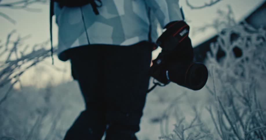Slow motion close-up of a photographer holding a camera while walking through a frosty, snow-covered landscape