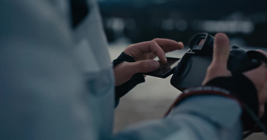 Over-the-shoulder view of a photographer adjusting the settings on a camera's touchscreen display outdoors