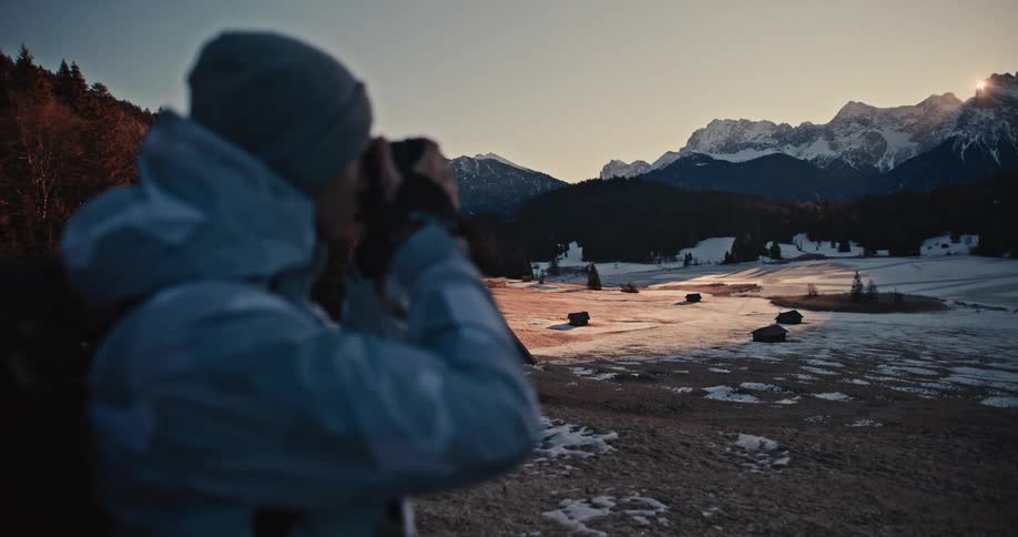 A photographer captures a beautiful sunset over a vast snowy mountain landscape with a frozen lake