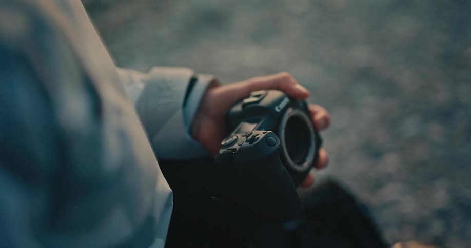 A close-up over-the-shoulder shot shows a photographer changing the lens on their camera in slow motion