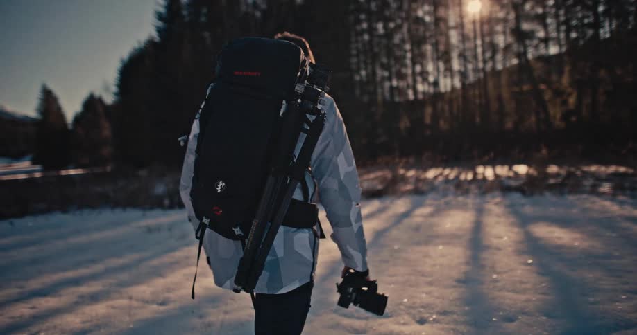 Cinematic slow motion shot of a male photographer walking through a snowy landscape during a beautiful sunset