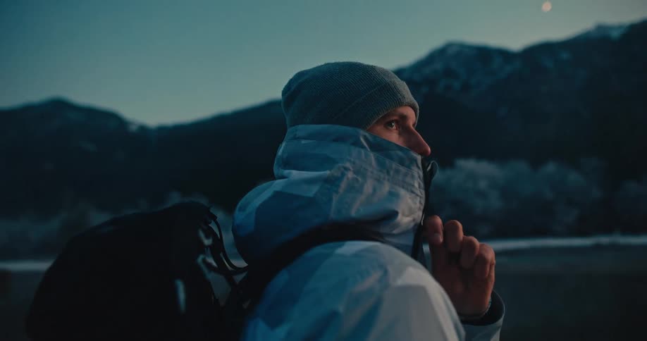 Close up of a lone hiker in winter gear observing a cold mountain landscape during the blue hour