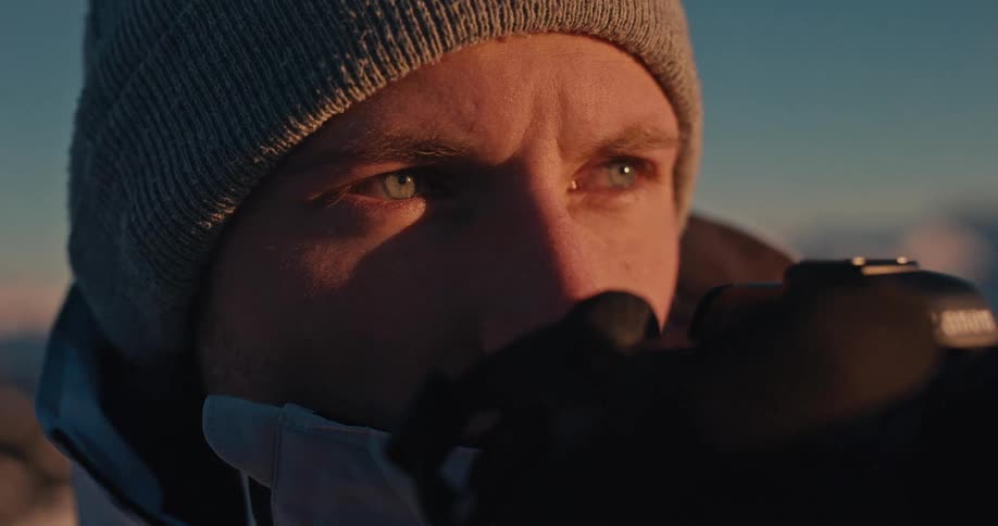 A close-up reveals a focused male photographer lowering his camera to survey the snowy landscape during a golden sunrise