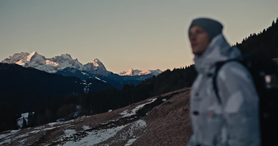 A male adventurer stops to take photos of the stunning mountain peaks at sunrise while on a winter hike