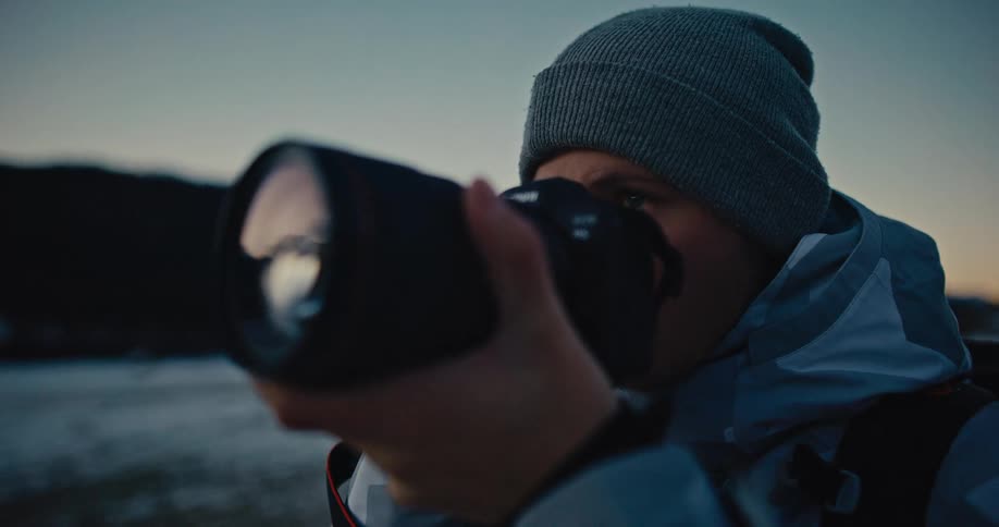 Close up of a photographer in winter gear capturing the serene landscape at dusk in slow motion