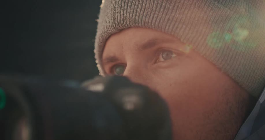 A close-up shot of a focused male photographer with blue eyes looking through his camera with a beautiful lens flare