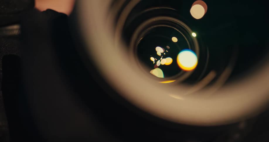 A cinematic macro shot of a camera lens as the aperture blades open and close, with colorful light reflections and bokeh