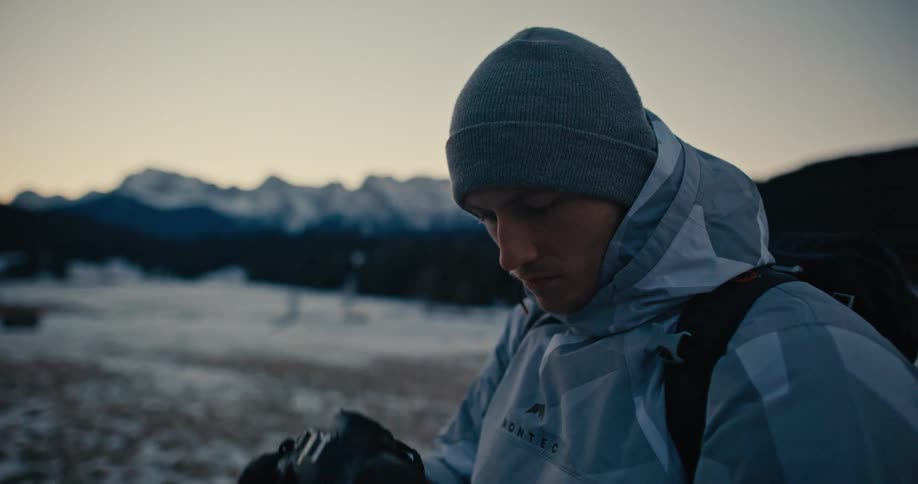 A photographer in winter gear captures the beauty of a snowy mountain range at dusk