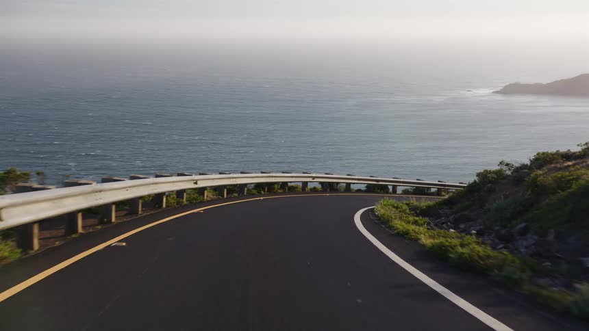 A serene point-of-view drive along a winding coastal highway overlooking a distant city and the vast ocean at golden hour