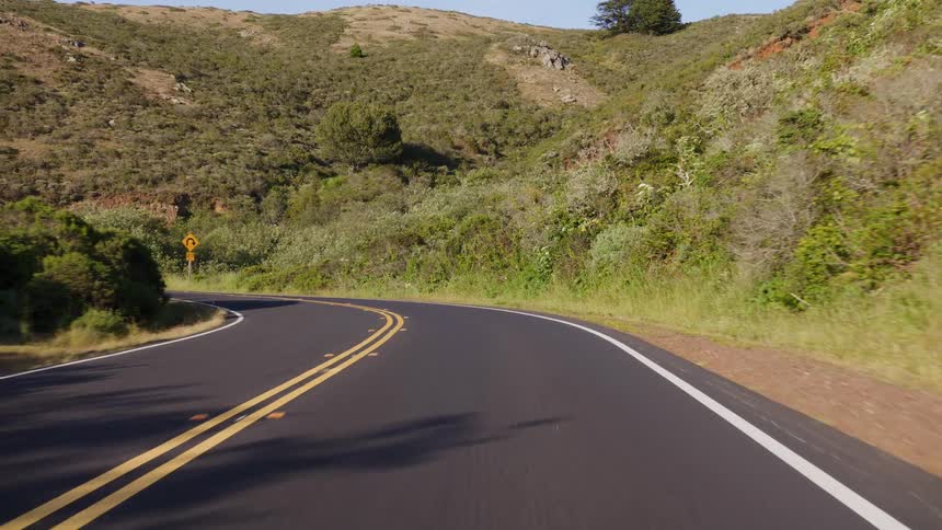 A smooth point-of-view drive navigates the sharp curves of a scenic mountain highway on a sunny day