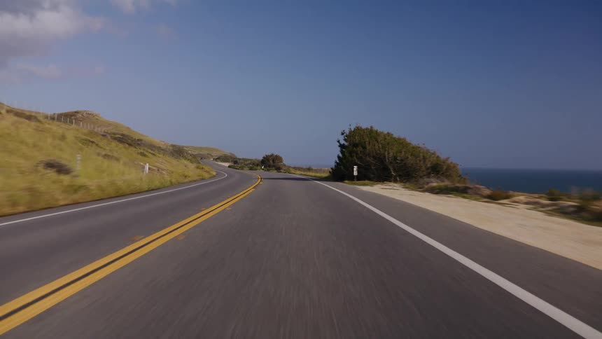 A scenic point-of-view drive along a winding coastal highway next to the ocean on a bright, sunny day