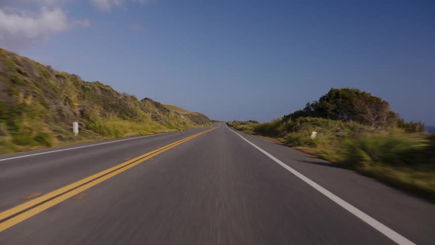 A point-of-view shot of a car driving along a winding coastal road on a sunny day