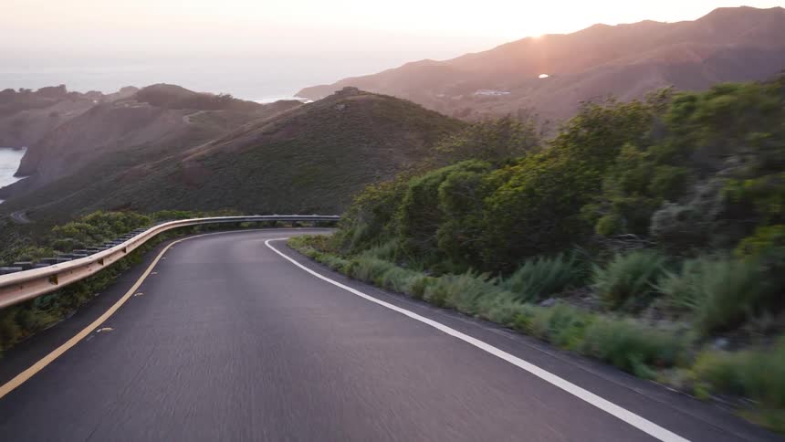 A point-of-view shot driving on a winding coastal mountain road during a scenic sunset