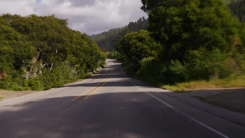 A scenic point-of-view drive down a quiet two-lane country road surrounded by lush green trees and rolling hills