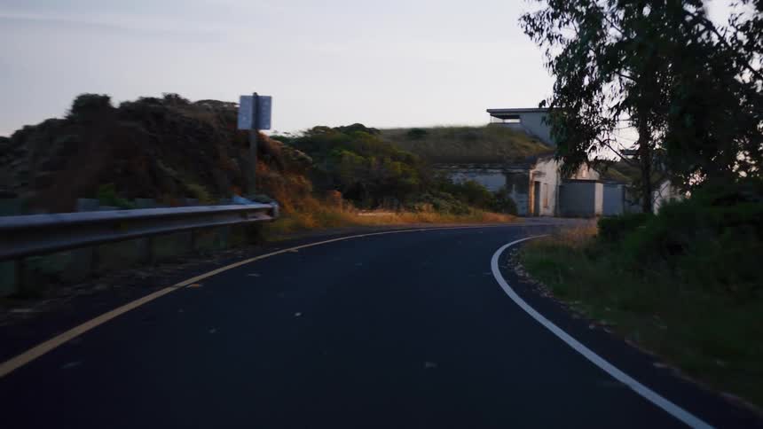 A point-of-view drive along a winding coastal road reveals abandoned military bunkers at sunset