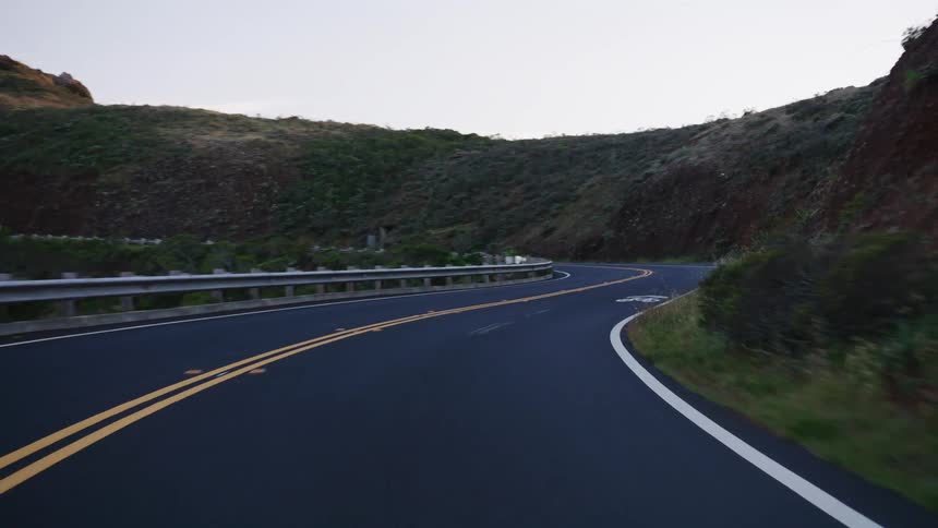 A serene point-of-view drive along a winding, empty mountain road at dusk, with green hills on either side