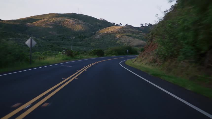 Driving a winding country road through rolling green hills as the golden hour sun shines on the landscape
